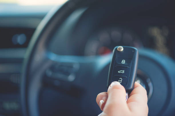 Woman holding a car key. The steering wheel and dashboard are in the background. She is about to press the key buttons. Close up with copy space.