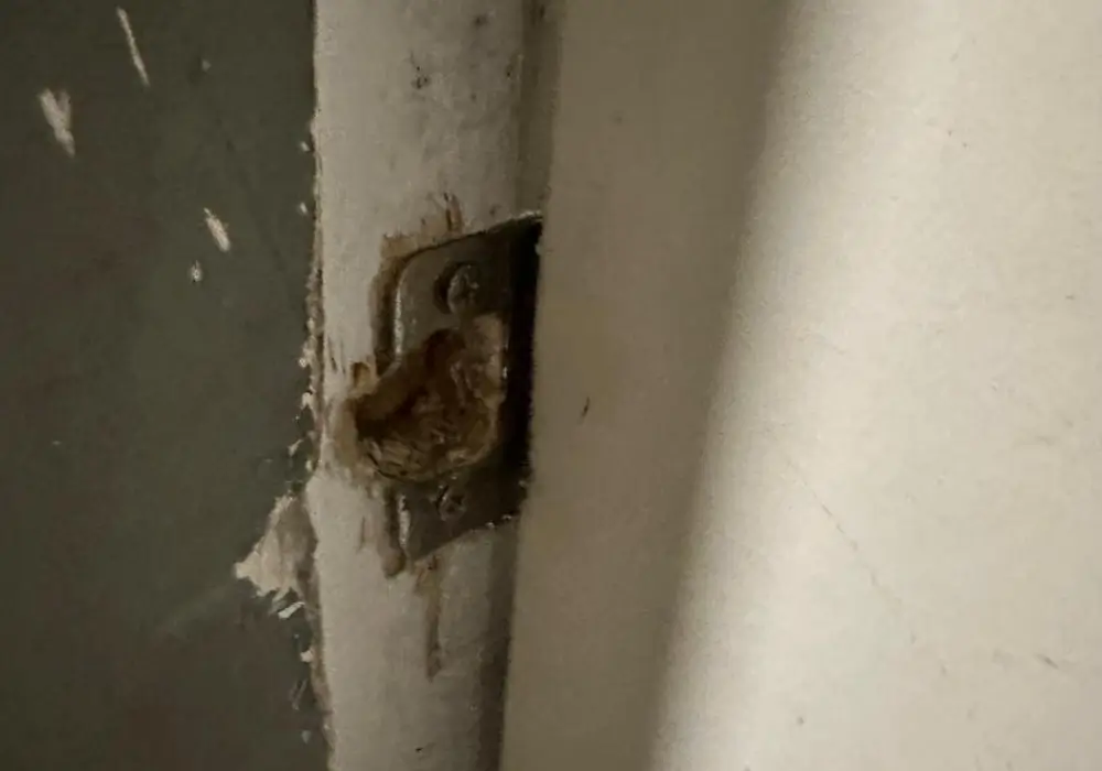Damaged door frame and strike plate after a forced entry attempt